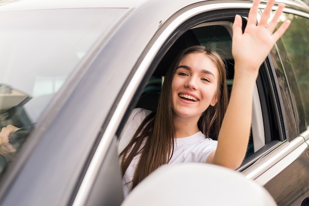 Hola. Hermosas mujeres jóvenes alegres con sonrisa y saludando mientras está sentado en su coche