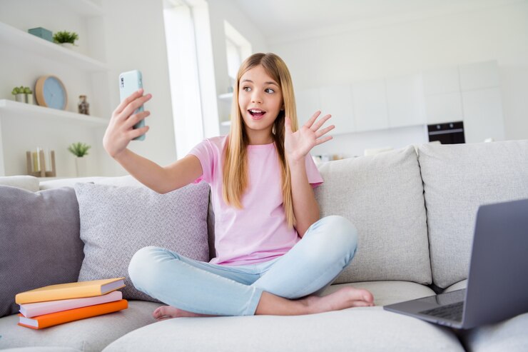 Hola seguidores. Foto de cuerpo entero de niño niña estudio remoto descanso relajarse usar teléfono inteligente tener transmisión de instagram en línea mano de onda decir hola sentarse piernas cruzadas cómodo sofá en casa en el interior