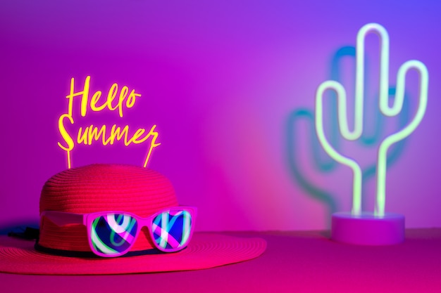 Foto hola verano con sombrero y gafas de sol luz de neón con cactus en rosa y azul en la mesa