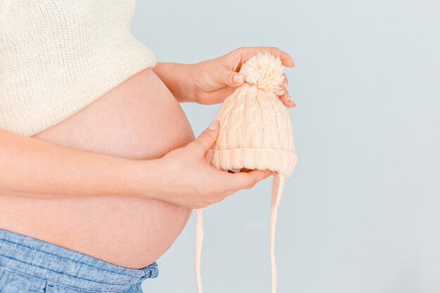 Holding der schwangeren Frau gestrickt nahe ihrem Bauch, der auf die Geburt des Kindes wartet