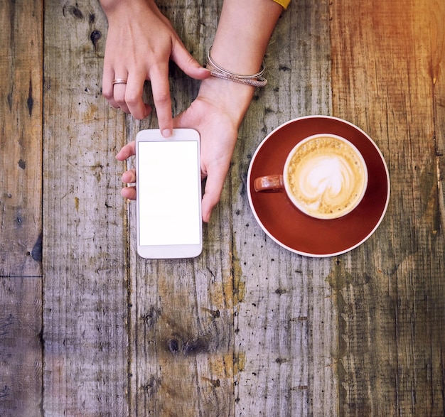 Holen Sie sich einen Kaffee und nehmen Sie an der Unterhaltung teil Hochwinkelaufnahme einer Frau, die ihr Handy benutzt und eine Tasse Kaffee trinkt