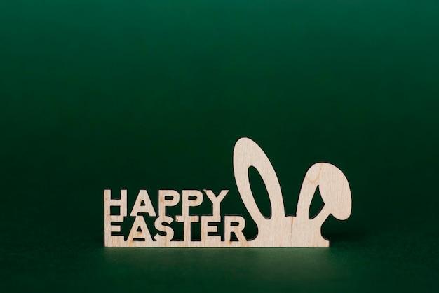 Holzaufschrift Frohe Ostern und stilisierte Hasenohren auf dunkelgrünem Hintergrund