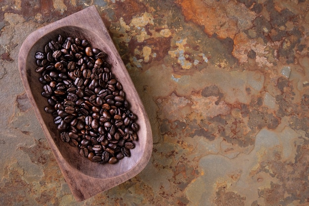 Holzbehälter mit gerösteten Kaffeebohnen auf rostigem Schiefer.