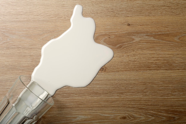 Holzboden mit umgekipptem Glas weißer Milch.