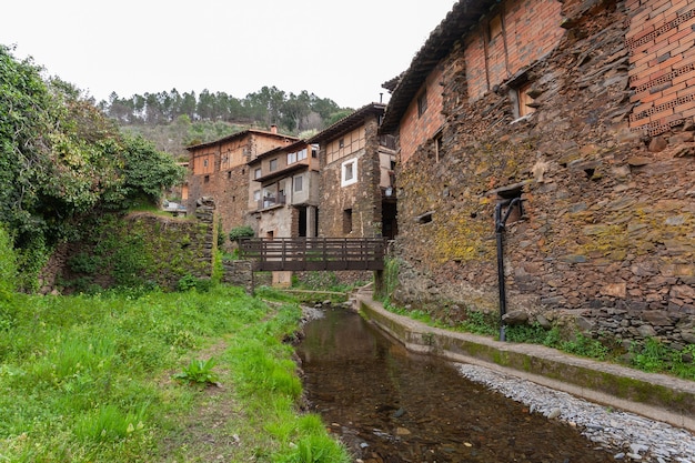 Holzbrücke zur Überquerung des Arrago-Flusses vor dem Hintergrund traditioneller Schiefer- und Lehmhäuser