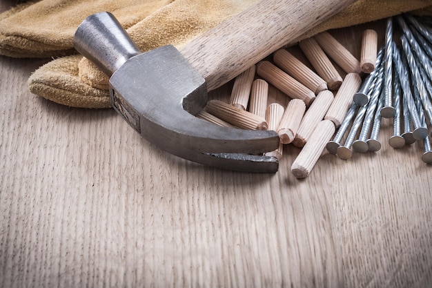 Holzdübel Klauenhammer Lederschutzhandschuhe und lange Baunägel auf Holzbrettwartungskonzept