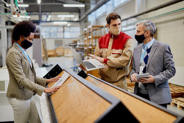 Holzfabrikarbeiter, der mit Inspektoren spricht, während er Laptop und Produktionsanlage benutzt