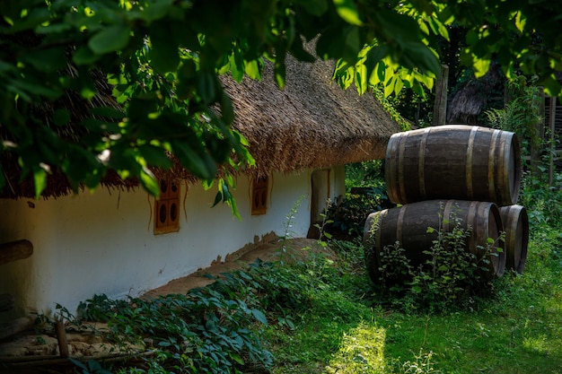 Holzfässer in der Nähe eines alten Hauses mit Strohdach. Hintergrund