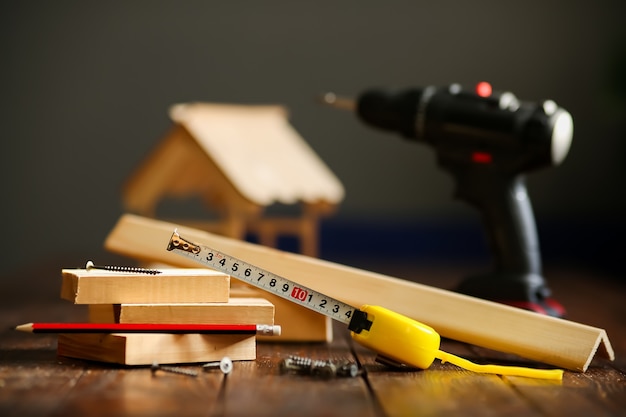 Holzhaus auf einer Holzoberfläche aus Brettern und Werkzeugen, Maßband, Schraubendreher, Bleistift. Konzept - Bau eines schlüsselfertigen Hauses. Hochwertiges Foto