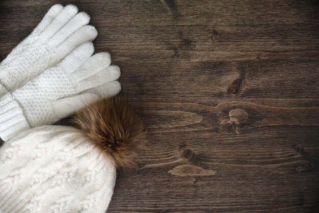 Holzhintergrund mit warmweißen Handschuhen und Hut mit Bommel