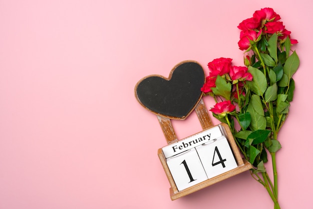 Holzkalender 14. Februar und Rosen auf rosa Hintergrund flach liegen