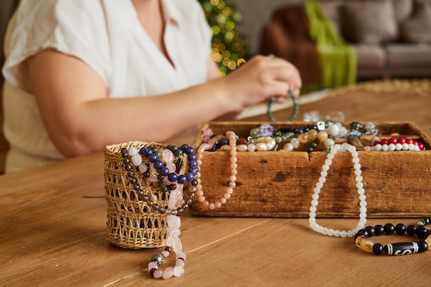 Holzkiste mit bunten Perlen, handgefertigte Edelsteinarmbänder, Hände einer Handwerkerin in Unschärfe.