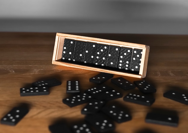 Holzkiste mit Domino-Spielsteinen und verstreuten Würfeln auf Holztisch