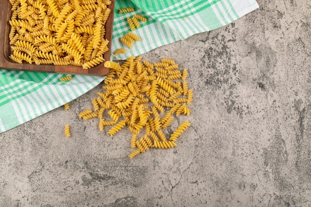 Holzkiste mit trockenen rohen Fusilli-Nudeln auf Steintisch.