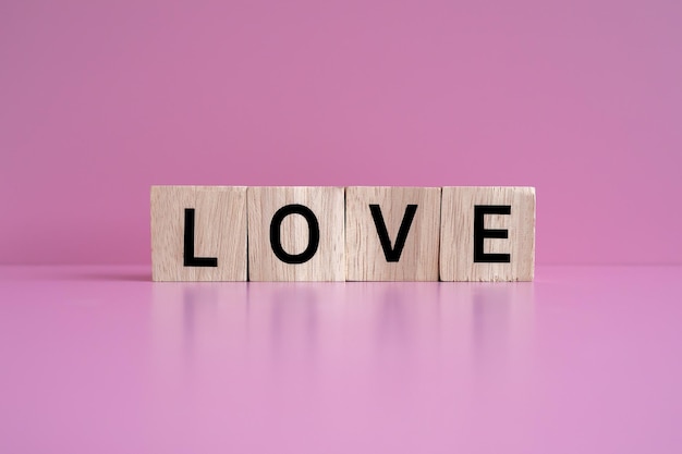 Holzklötze bilden den Text LOVE vor einem rosa Hintergrund