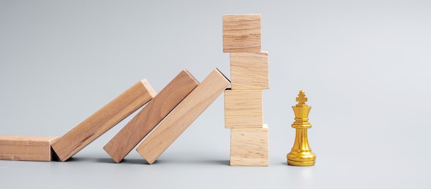 Holzklötze oder Dominosteine fallen auf goldene Schachkönigfigur