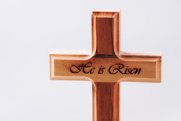 Holzkreuz mit Text Er ist auf dem grauen Hintergrund auferstanden Erinnerung an das Opfer Jesu und die Auferstehung Christi Ostern Eucharistiekonzept Christentum Symbol und Glaube