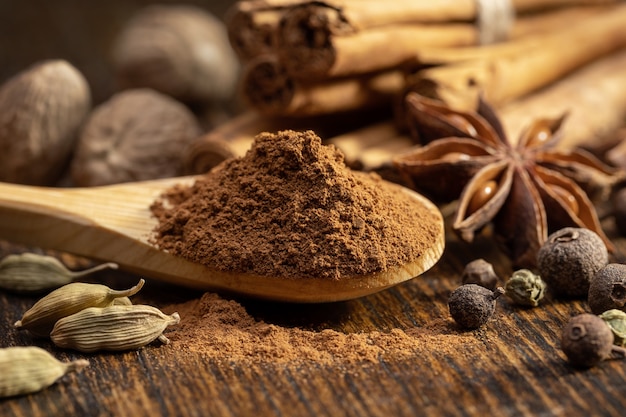 Holzlöffel mit gemahlenem Zimt und Zimtschnecken Ganze Muskatnüsse Cordamom Anis Piment Erbsen Eine Reihe von Gewürzen auf einem braunen Tisch