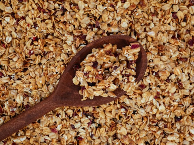 Holzlöffel mit hausgemachtem, geröstetem Bio-Müsli mit Preiselbeeren auf Müsli-Textur. Essen zum Frühstück, Mahlzeithintergrund