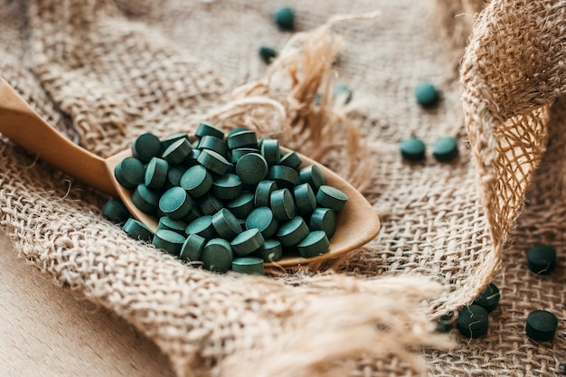 Holzlöffel mit Spirulina-Tabletten vor dem Hintergrund der Sackleinen