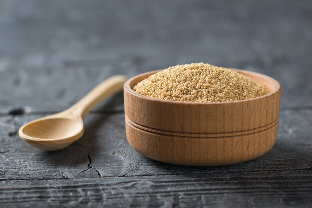 Holzlöffel und Holzschale mit Amaranth-Samen auf schwarzem rustikalem Tisch.