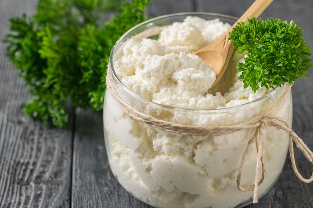 Holzlöffel und Petersilienblätter in einem Glas mit frischem Hüttenkäse.