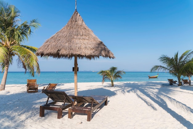 Holzlounge unter strohgedecktem Sonnenschirm am Strand im tropischen Meer auf der Insel Lipe. Sommer- und Urlaubskonzept