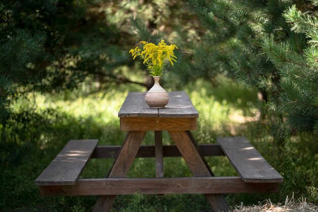 Holzmöbel im Garten im Freien. Einfache Bänke und Esstisch mit Strauß gelber Blumen