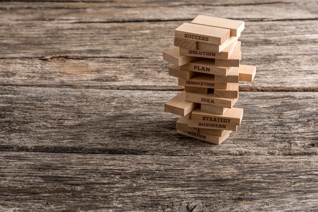 Foto holzpflöcke sind in einen turm eingebaut, von denen einige wörter lesen, die die wichtigsten elemente auf dem weg zum geschäftserfolg darstellen - vision, strategie, idee, innovation, plan und lösung.