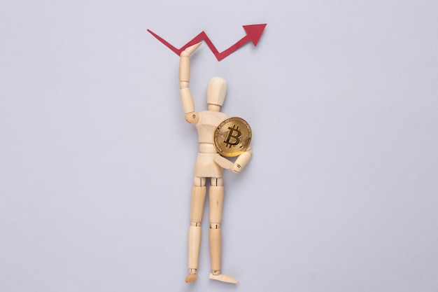 Holzpuppe mit Bitcoin und Wachstumspfeil auf grauem Hintergrund Kryptowährung Der Anstieg des Bitcoin-Wertes