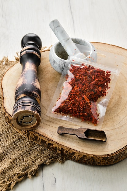 Holzquerschnitt mit zerkleinertem Paprika in Plastikverpackung und Steinmörtel und Mühle