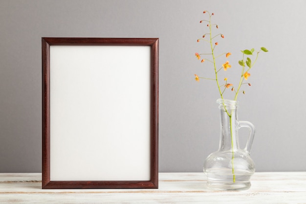 Holzrahmen mit orangefarbenen Barrenwort-Blüten im Glas auf grauem Pastellhintergrund. Platz kopieren,