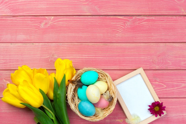 Holzrahmen mit Ostereiern und Tulpen auf buntem Hintergrund