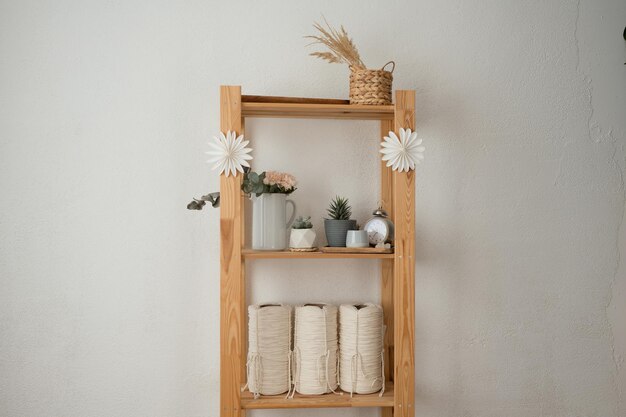 Holzregal mit Blumen und mit Rollen aus weißem Seil auf weißer Wand Innenarchitektur