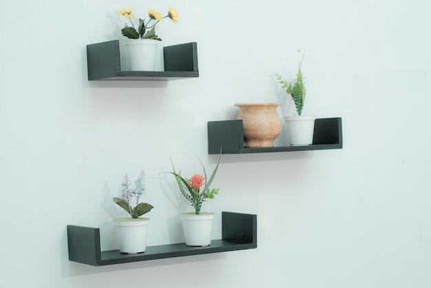 Holzregalen mit schönen Pflanzen, Wecker, Spielzeugwagen und Bücher an einer hellen Wand