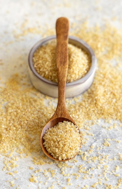 Holzschaufel und Schüssel mit trockenem, ungekochtem Bulgur-Weizenkorn aus nächster Nähe Gesundes Essen