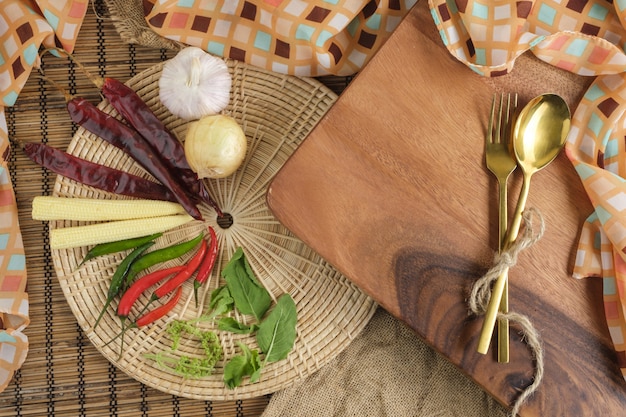 Holzschneidebrett mit thailändischen Kräutern und Löffel und Gabel mit freiem Platz für Texthintergrund