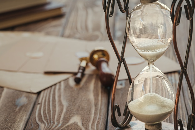 Foto holzschreibtisch mit vintage sanduhr und altem brief mit bodensiegel