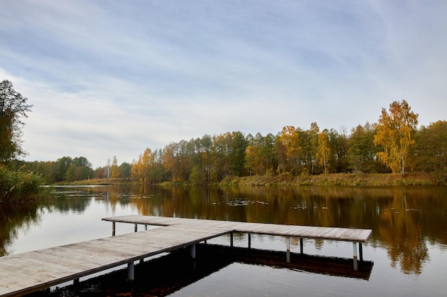 Holzsteg zum Festmachen von Booten am Flussufer in der Nähe des Herbstwaldes.