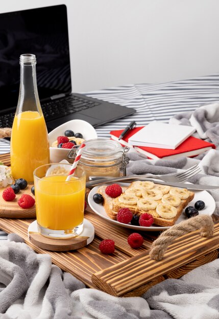 Holztablett mit Glas Orangensaft und Sandwich mit Beeren auf dem Bett