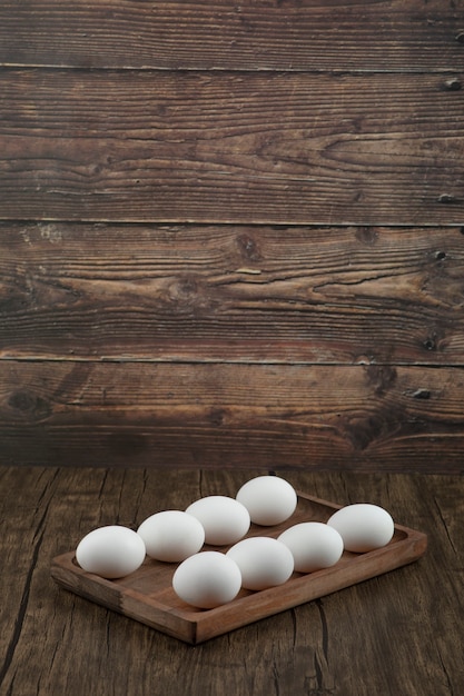 Holzteller mit rohen weißen Eiern auf Holztisch.