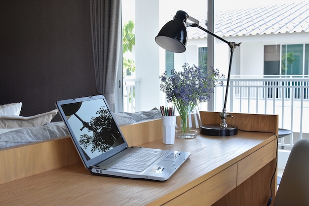 Holztisch mit Computernotizbuch, -bleistift, -lampe und -blumen im modernen Arbeitsbereich