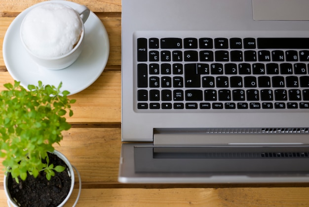 Holztisch mit Laptop-Computer Kaffeetasse und Blume