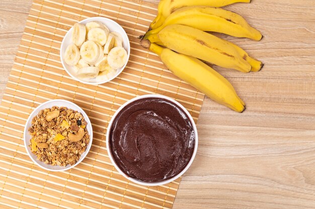 Holztisch mit leckerem Acai-Topf. Kleine Töpfe mit Granalo und Banane.