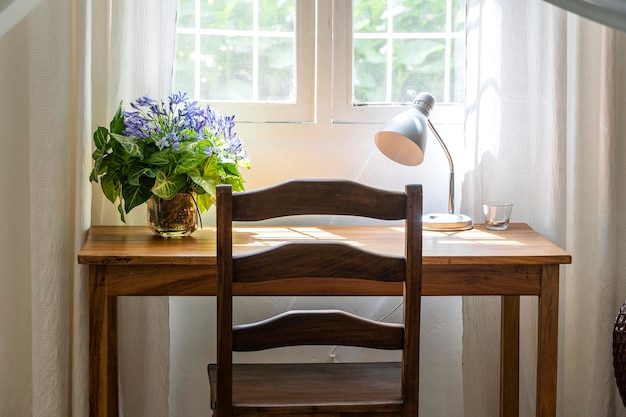 Holztisch mit Stuhllampe und Blumenstrauß am Fenster im modernen Arbeitsbereich zu Hause