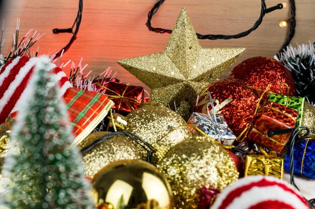 Holztisch mit Weihnachtsschmuck. Rote, silberne und goldene Kugeln, Geschenkboxen, Lichter, Panettone, Weihnachtsbaum und andere. Selektiver Fokus.