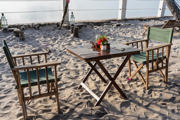 Holztisch und zwei Stühle am Meer am tropischen Strand bei Sonnenuntergang Das Konzept eines romantischen Abendessens