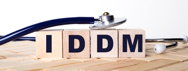 Holzwürfel mit dem Wort IDDM auf einem hölzernen Hintergrund und einem Stethoskop auf ihnen. Medizinisches Konzept