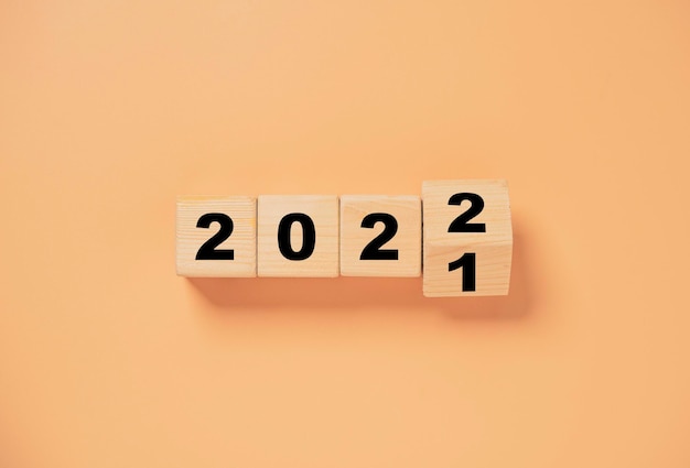 Holzwürfelblock, der von 2021 bis 2022 auf orangefarbenem Hintergrund kippt, Vorbereitung auf frohe Weihnachten und ein glückliches neues Jahr.