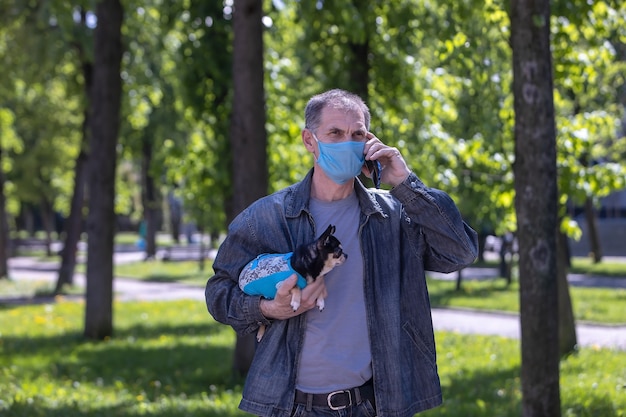 Un hombre de 50 años con una máscara protectora con un perro en el parque y hablando por un teléfono móvil